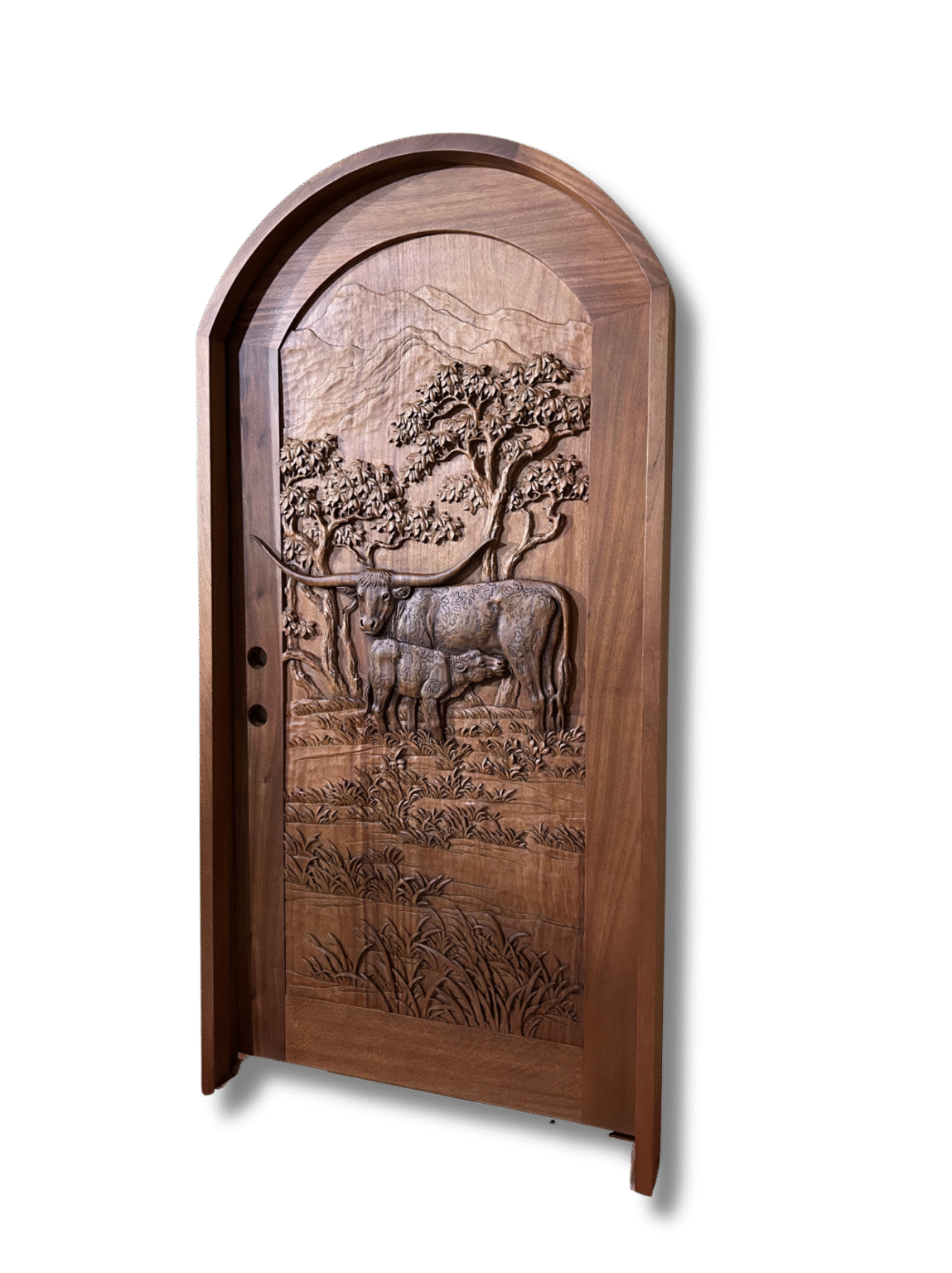 Angled studio shot on a black background displaying a round-top arched solid wood single entry door with a high-relief hand-carving of a Texas Longhorn cow nursing her calf set against a landscape with oak trees and mountains.