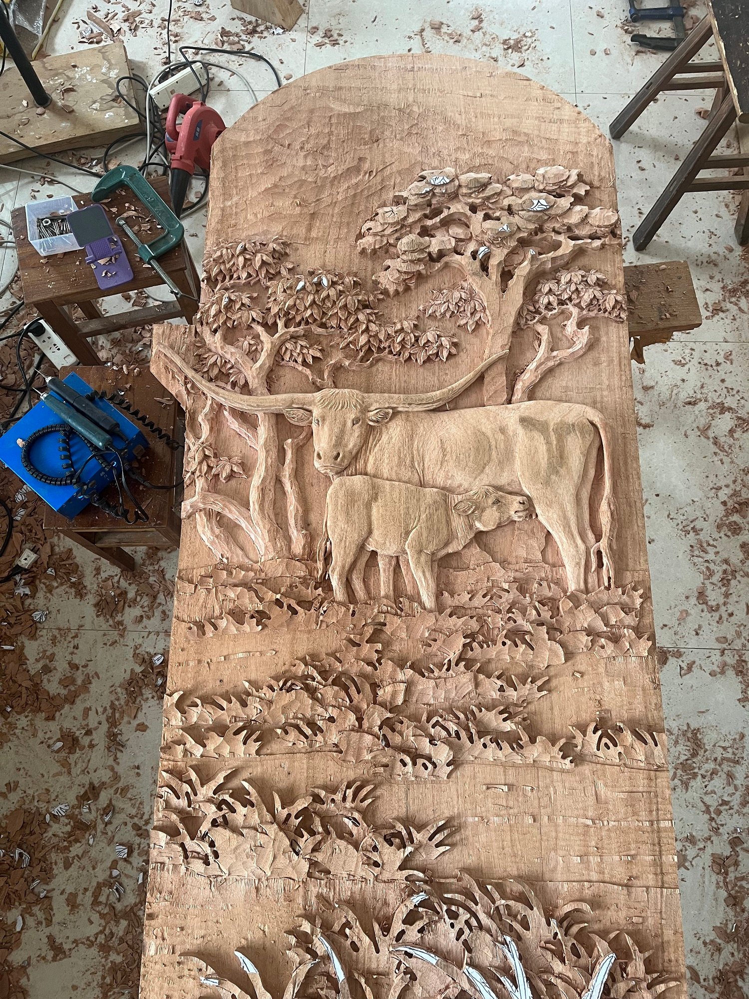 High-relief hand-carved solid wood door panel featuring a Texas longhorn cow nursing her calf amid detailed trees and foliage, custom luxury entry door by Crown Custom Doors