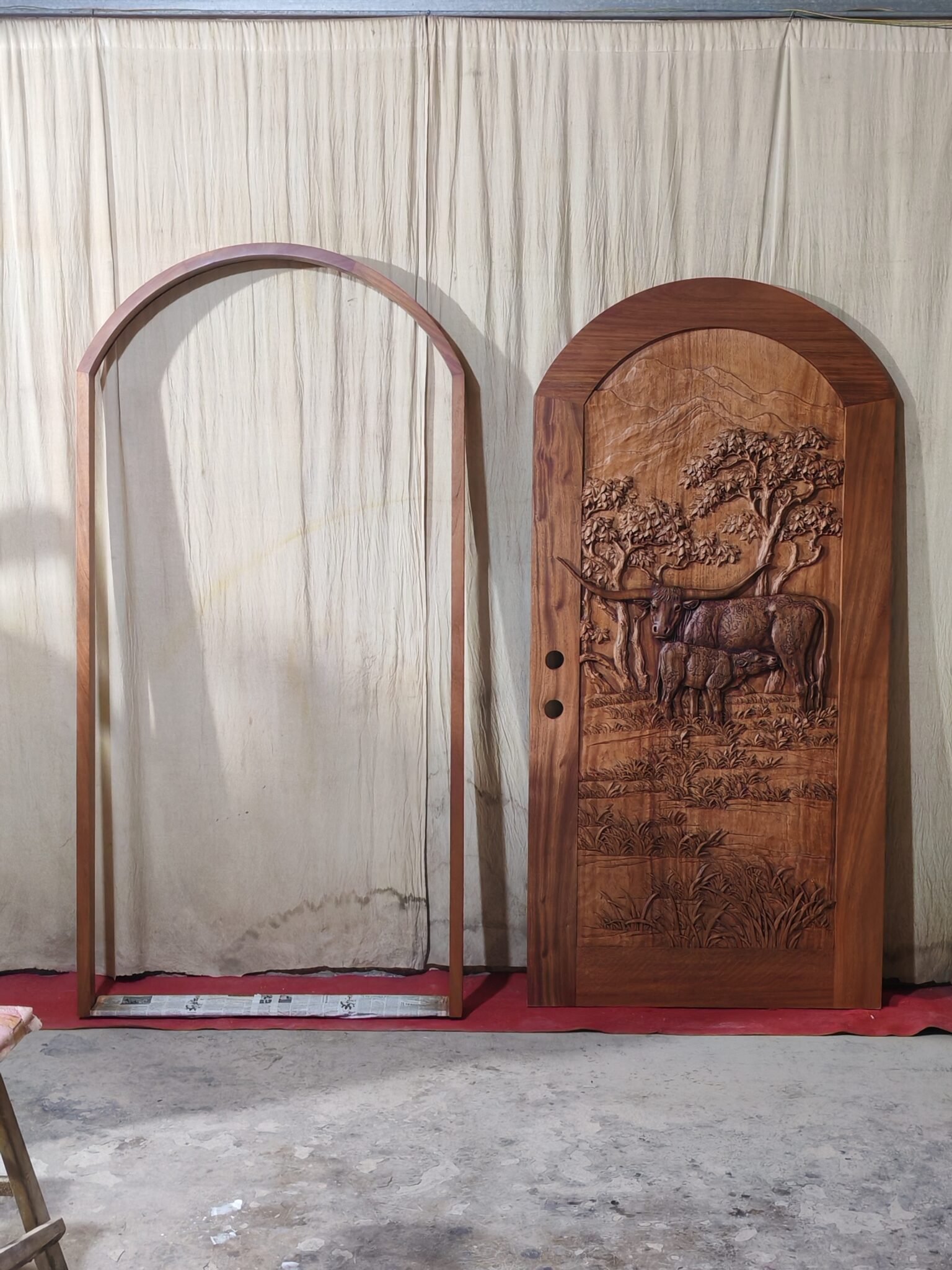 Full-length wide view of a finished round-top arched solid wood single entry door standing next to its standalone matching arched door jamb frame set against a neutral studio backdrop for a Texas ranch home.