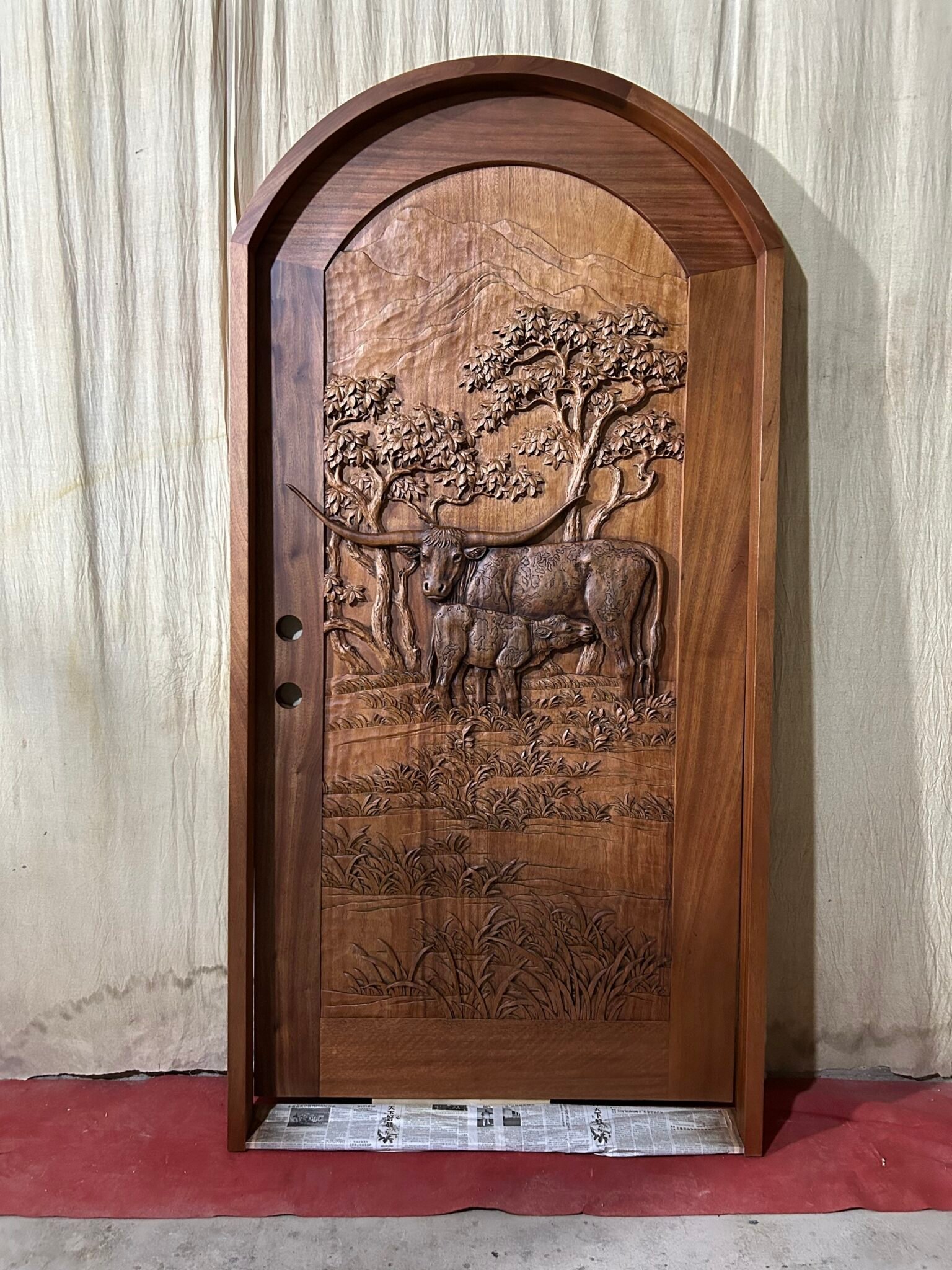 Full front view of a finished round-top arched solid wood single entry door set inside its matching wood door jamb frame, featuring a hand-carved Texas Longhorn cattle motif for a Texas ranch home.