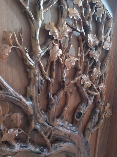 Crown Custom Doors angled perspective showing deep three-dimensional relief carvings of intertwining oak tree branches and dense foliage on a solid wood door.