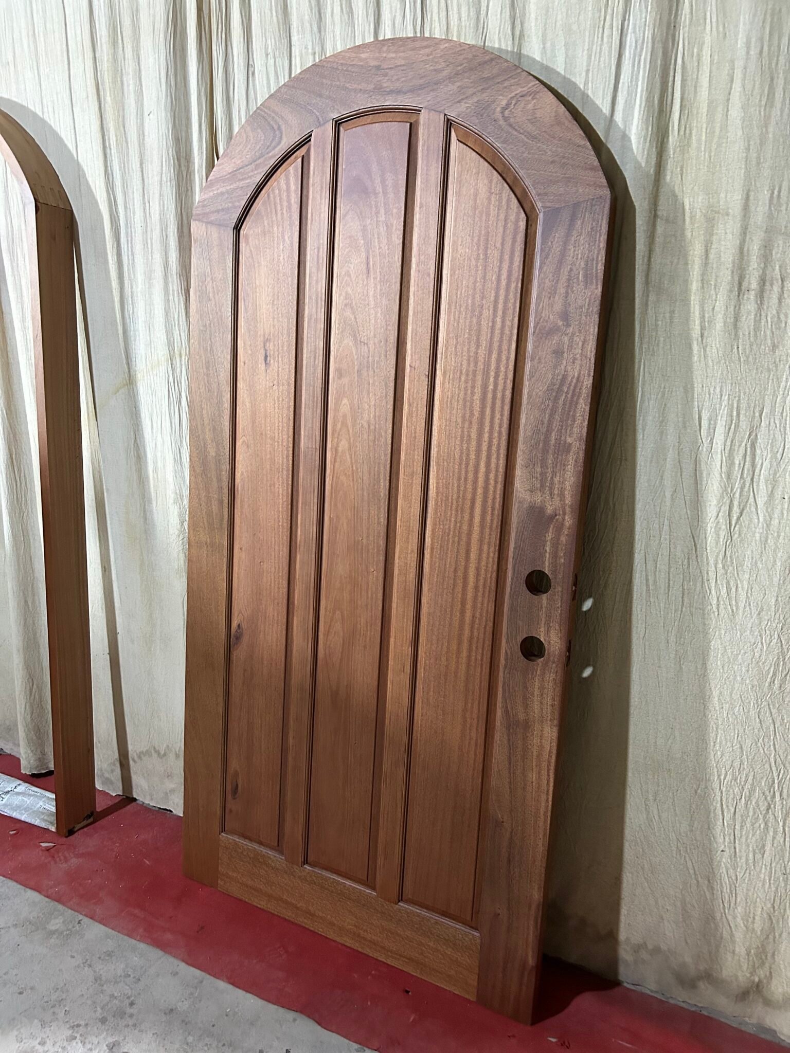 Angled view of the interior backside of a finished round-top arched solid wood single entry door, displaying smooth vertical plank panels and natural wood grain for a Texas ranch home.