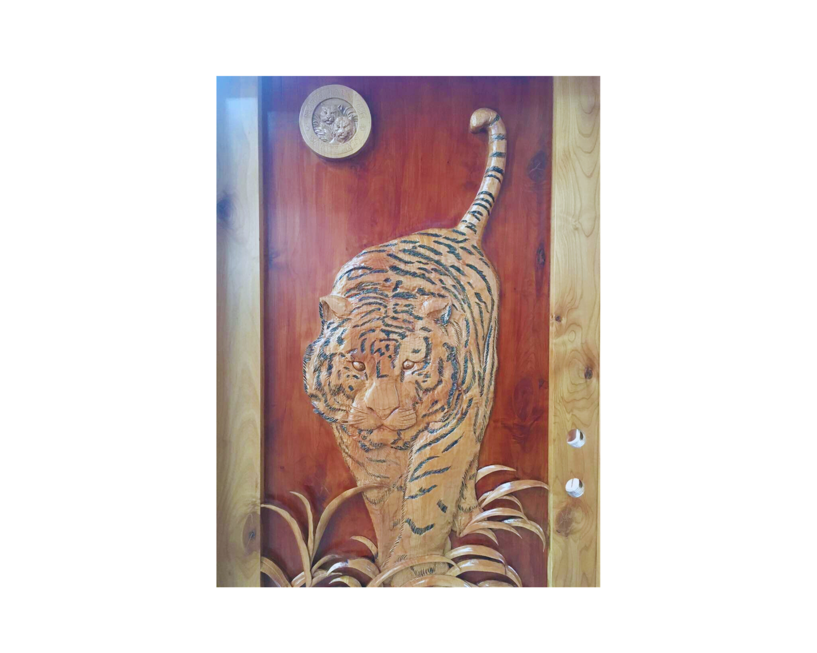Detailed close-up of a custom hand-carved solid wood entry door titled Tiger's Gaze, featuring a 3D relief carving of a tiger walking through tall grass with an official sanctuary emblem seal, crafted by Crown Custom Doors.