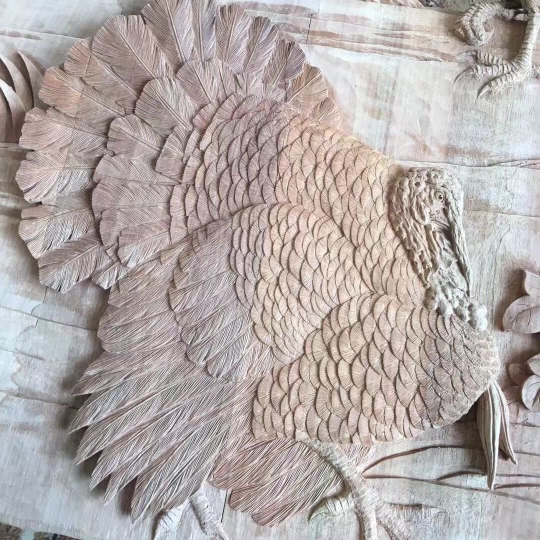 Overhead view of a raw solid wood door panel showing a fully carved, high-relief wild turkey with fanned tail feathers, detailed plumage, and carved talons in progress on the workshop workbench.