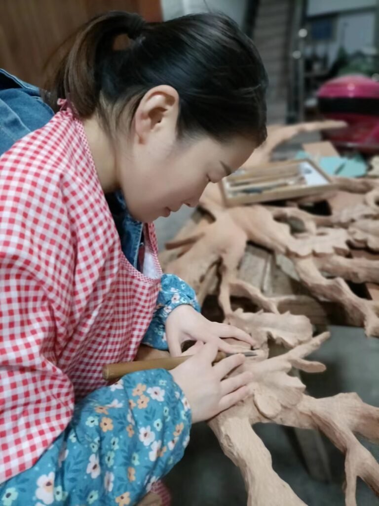 Artisan woodcarver refining hand-carved oak leaves and tree branch details on a solid wood door panel using traditional carving tools.