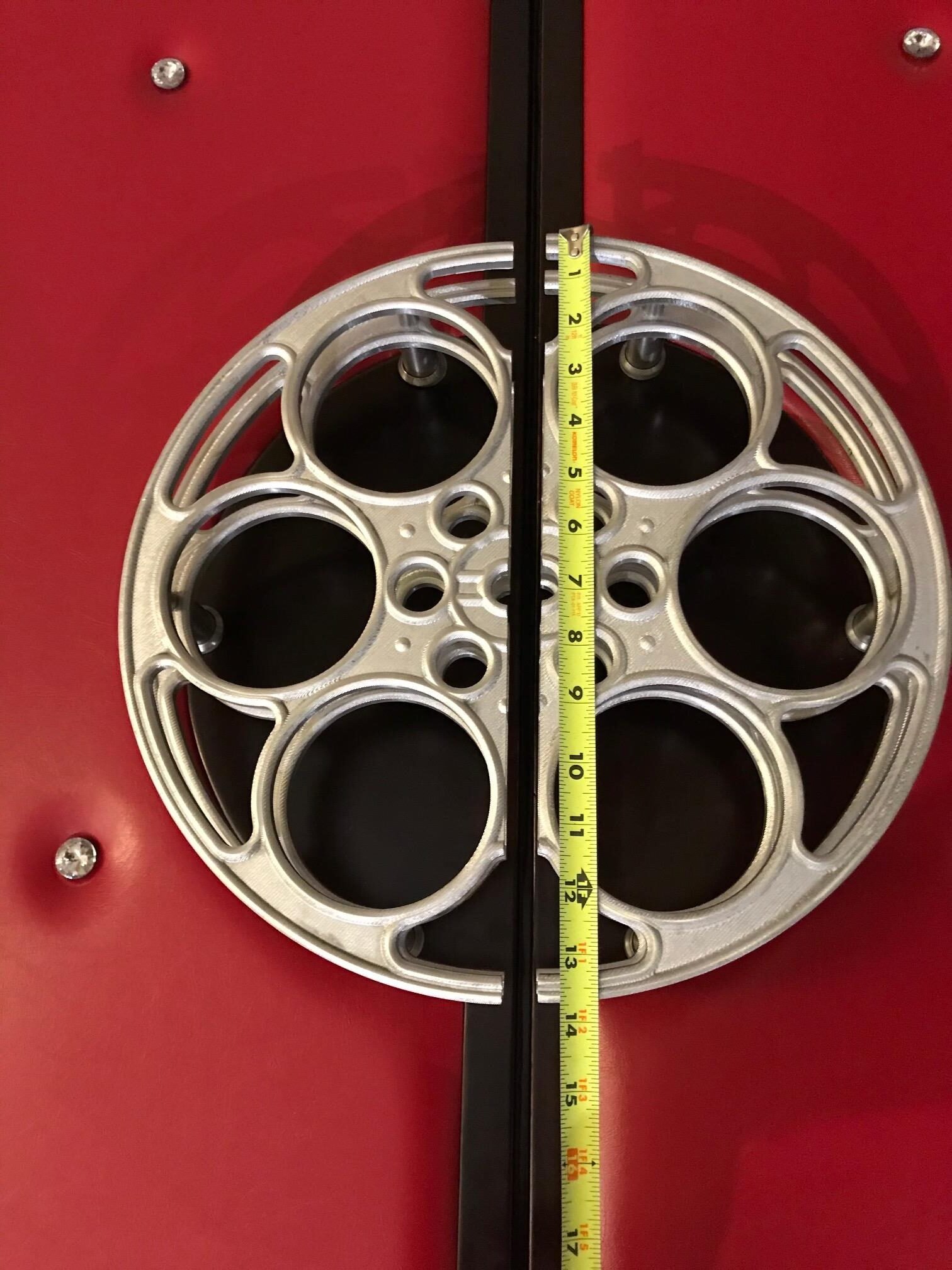 A yellow measuring tape laid over a pair of 14-inch silver metallic film reel door pull handles mounted on red upholstered acoustic double doors.