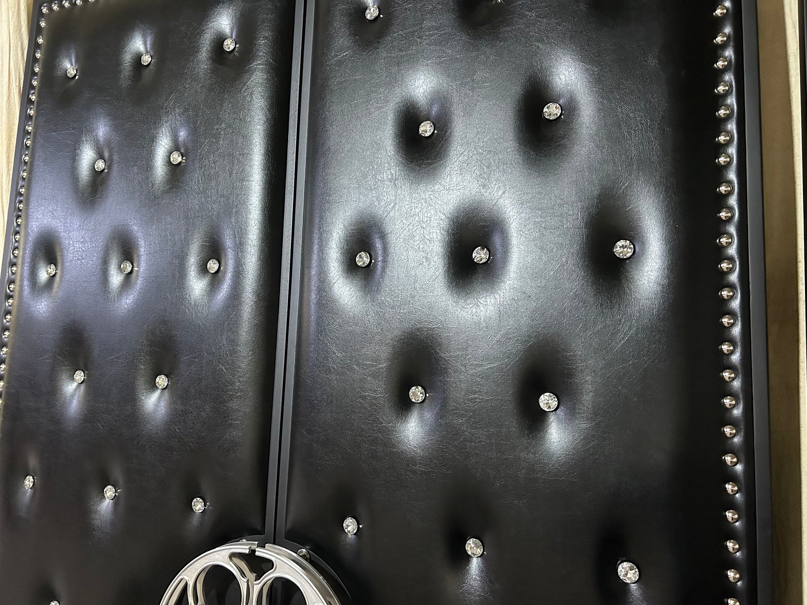 Close-up view of custom acoustic home theater double doors showing black diamond-tufted vinyl upholstery with sparkling crystal buttons and silver stud border trimming by CROWNCUSTOMDOORS.