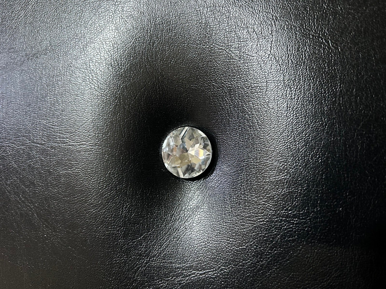 Extreme close-up macro view of a clear faceted crystal diamond button set into black tufted leather-grain vinyl upholstery on a custom acoustic home theater door by CROWNCUSTOMDOORS.