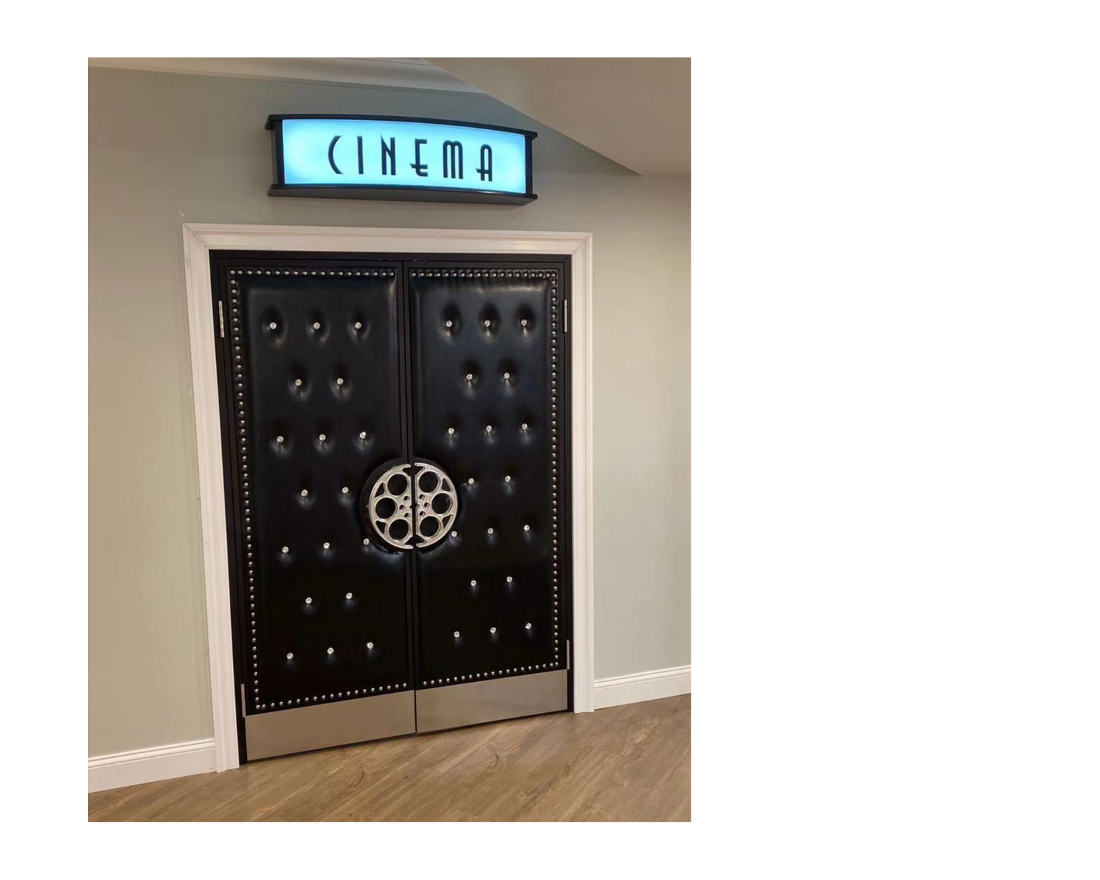 Installed custom black button-tufted vinyl acoustic home theater double doors featuring silver nailhead trim, circular silver film reel center handles, silver kickplates, and an illuminated CINEMA sign mounted above the frame.
