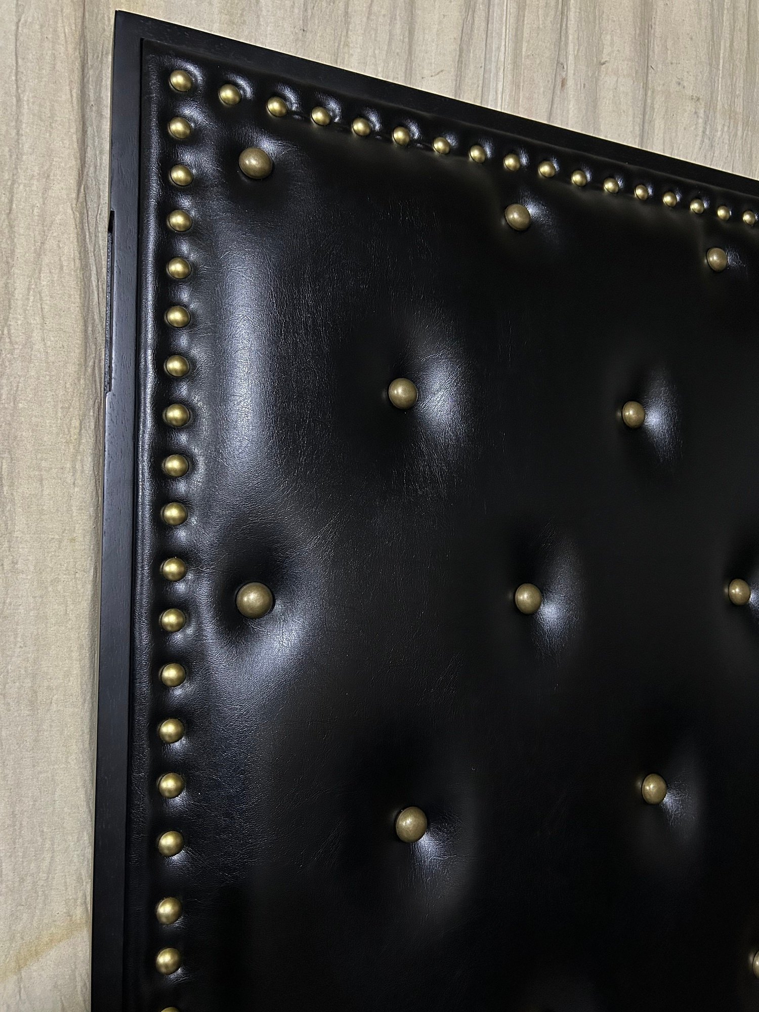 Detailed close-up of the upper corner on a black vinyl upholstered theater door showing a row of decorative brass perimeter studs and deep-set antique bronze mushroom tufting buttons.