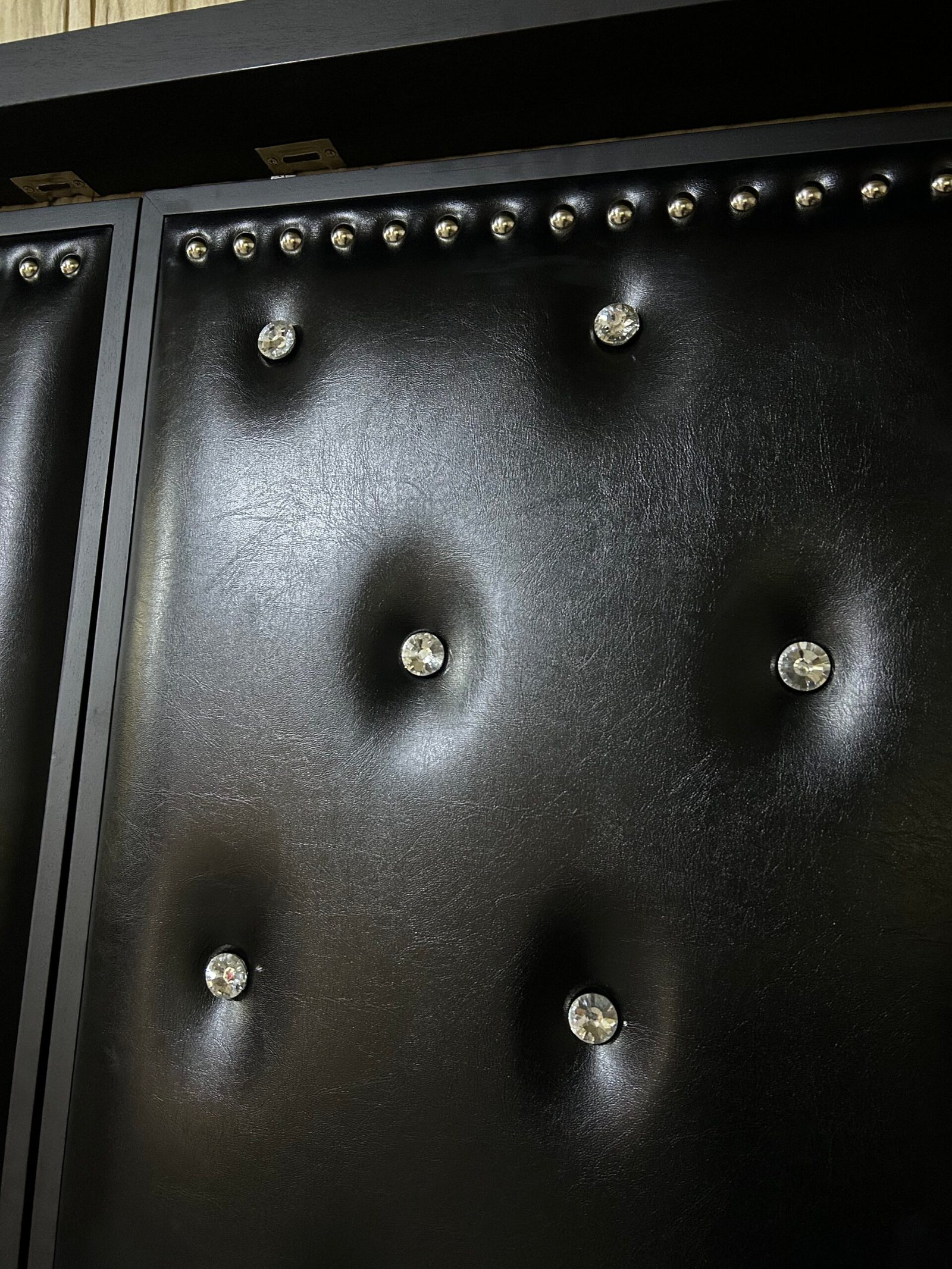 Close-up of black leatherette upholstered home theater door panel featuring deep diamond tufting with sparkling crystal buttons and silver stud trim along the top frame.