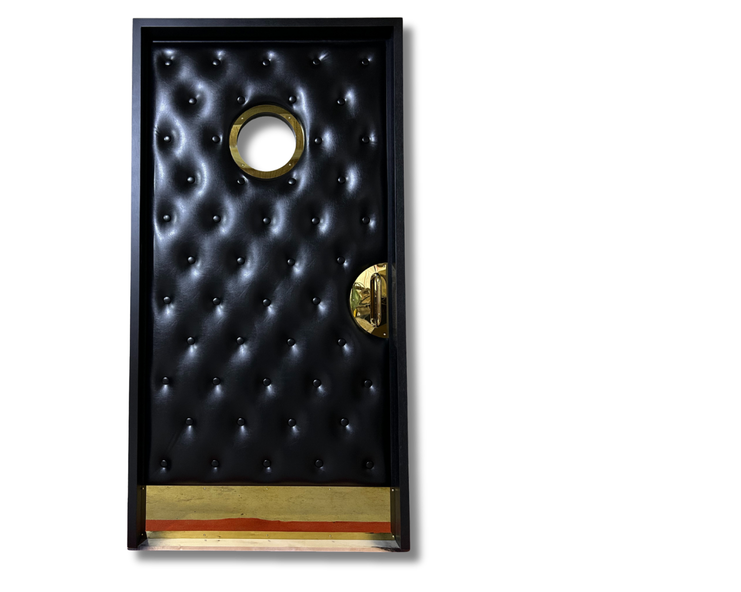 Custom acoustic home theater door with black button-tufted upholstery, circular brass porthole window, half-moon pull handle, and brass kickplate set against a solid black background.