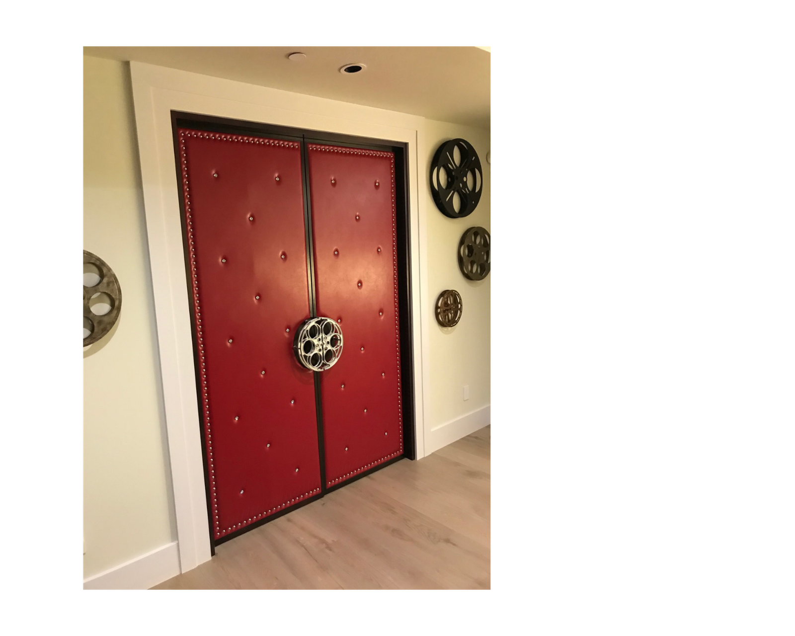 Custom soundproof double home theater doors with red button-tufted leather upholstery, silver stud trim border, and a silver film reel center pull handle installed in a home cinema entry.