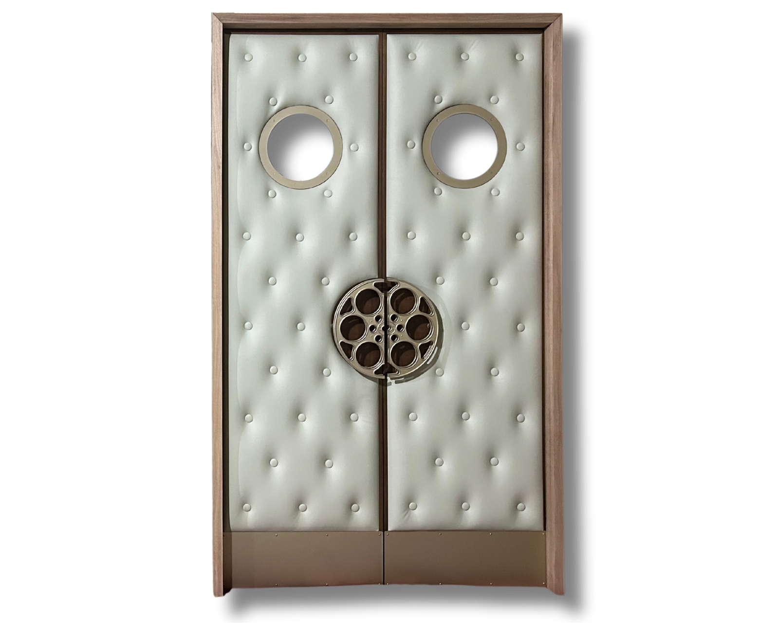 Full front view of custom off-white cream button-tufted acoustic home theater double doors featuring brass porthole vision windows, custom brass film reel pull handles, and kick plates set in a natural wood frame by Crown Custom Doors.