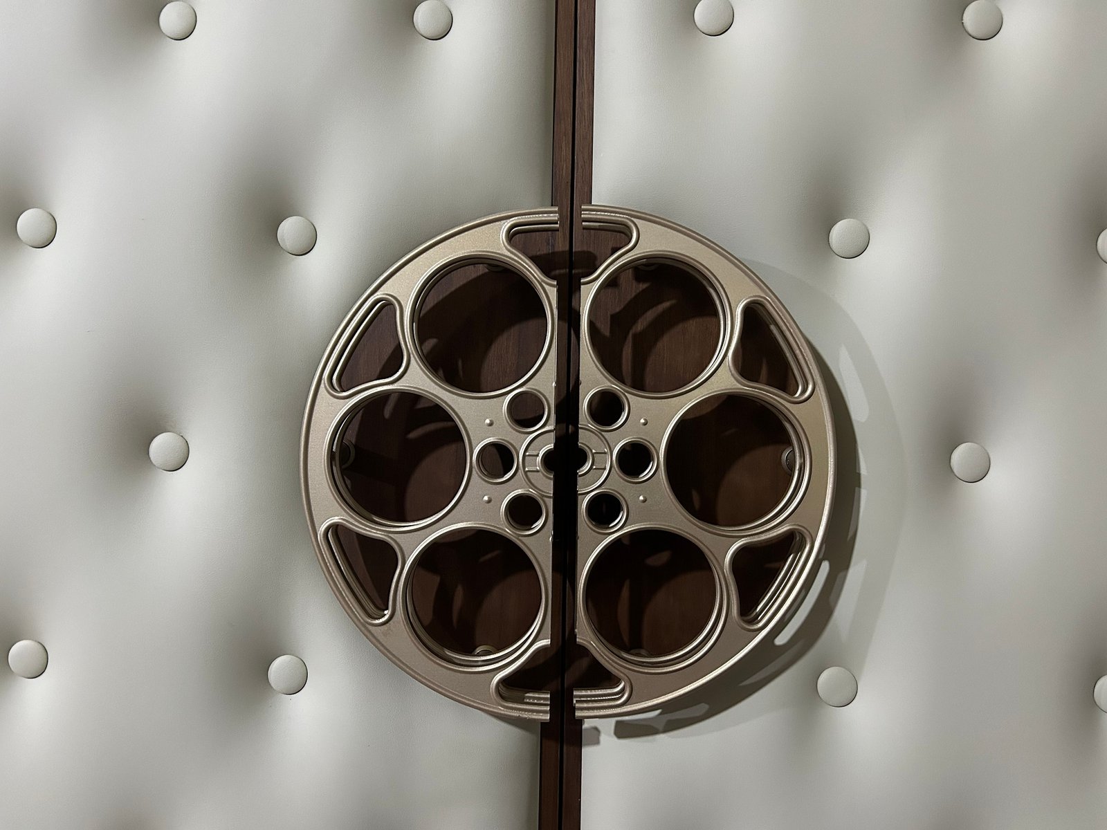 Close-up detail of off-white button-tufted vinyl upholstered acoustic double doors featuring custom brass film reel pull handles by Crown Custom Doors.