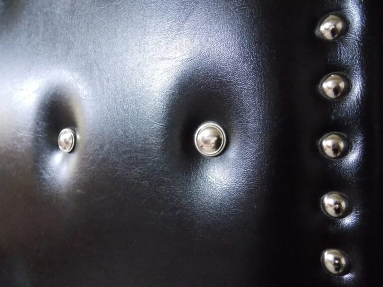Extreme close-up detail of tufted black leatherette vinyl upholstery featuring silver accent buttons and lined decorative silver tack studs on a custom soundproof home theater door by Crown Custom Doors.