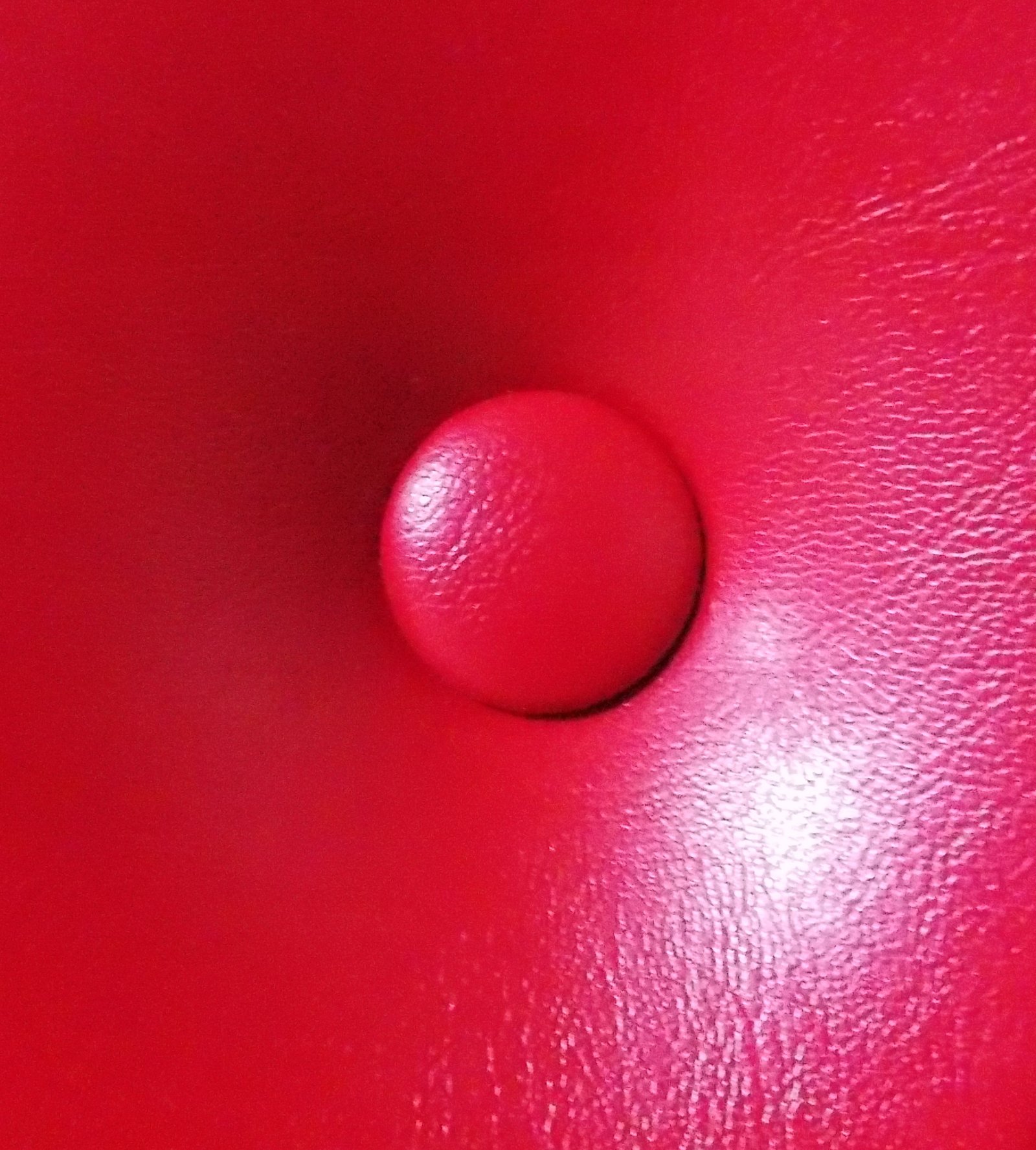 Extreme close-up macro view of a matching wine red vinyl covered button tufted into textured leatherette upholstery on an acoustic home theater door.